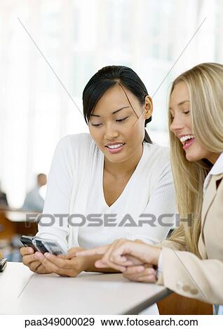 Two young business women looking at cell phone together View Large Photo Image Stock Photo - Two young business women looking at cell phone together. Fotosearch