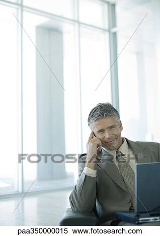 Businessman using cell phone and laptop in lobby View Large Photo Image Stock Photography - Businessman using cell phone and laptop in lobby. Fotosearch