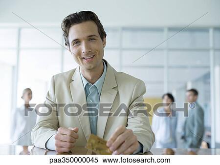 Man holding out credit card at reception desk, looking at camera View Large Photo Image Stock Photography - Man holding out credit card at reception desk, looking at camera. Fotosearch
