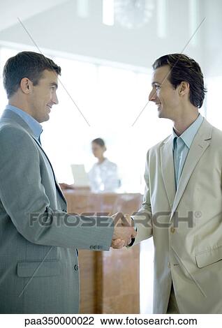 Two businessmen shaking hands in lobby View Large Photo Image Stock Image - Two businessmen shaking hands in lobby. Fotosearch