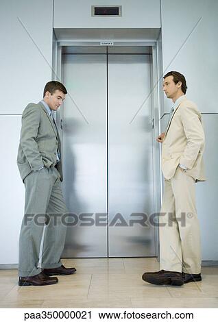 Stock Image - Two businessmen waiting by elevator door. Fotosearch