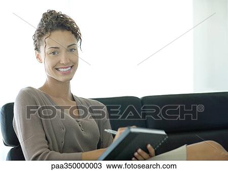 Woman writing in notebook, smiling at camera View Large Photo Image Stock Image - Woman writing in notebook, smiling at camera. Fotosearch