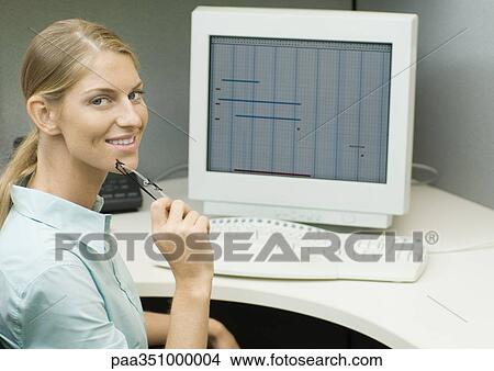 Female office worker sitting at computer, smiling at camera View Large Photo Image Picture - Female office worker sitting at computer, smiling at camera. Fotosearch