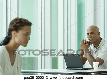 Man sitting with laptop, looking at female co-worker View Large Photo Image Stock Image - Man sitting with laptop, looking at female co-worker. Fotosearch