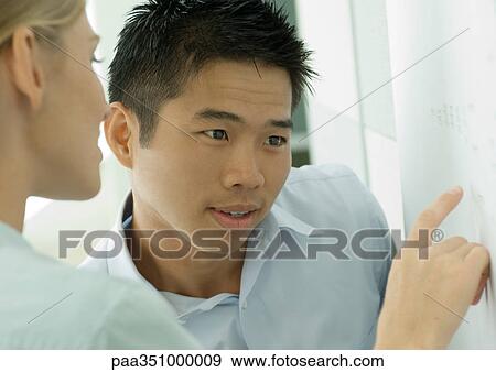 Stock Photo - Two co-workers looking at document on wall. Fotosearch
