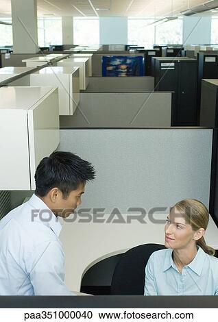 Stock Image - Two office workers talking in cubicle. Fotosearch