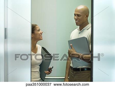 Two office workers with files talking in closing elevator View Large Photo Image Stock Photo - Two office workers with files talking in closing elevator. Fotosearch