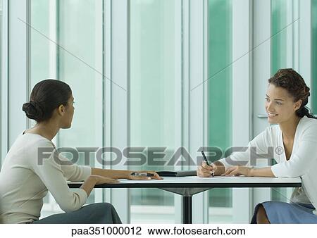 Two women sitting across from each other at table, working View Large Photo Image Stock Image - Two women sitting across from each other at table, working. Fotosearch