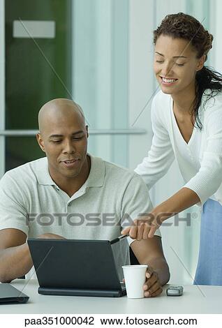 Woman leaning over man's shoulder, pointing to laptop screen View Large Photo Image Stock Image - Woman leaning over man's shoulder, pointing to laptop screen. Fotosearch