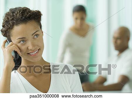 Woman using cell phone, colleagues in background View Large Photo Image Stock Photo - Woman using cell phone, colleagues in background. Fotosearch