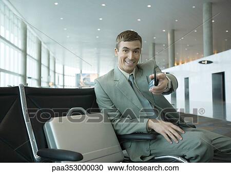 Businessman sitting in airport lounge, holding out cell phone toward camera View Large Photo Image Stock Image - Businessman sitting in airport lounge, holding out cell phone toward camera. Fotosearch
