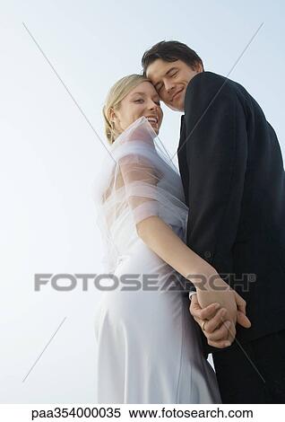 Bride and groom standing close together, holding hands, low angle view View Large Photo Image Stock Photography - Bride and groom standing close together, holding hands, low angle view. Fotosearch