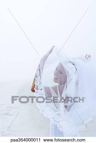 Bride holding up veil on beach View Large Photo Image Stock Image - Bride holding up veil on beach. Fotosearch