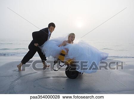 Groom pushing bride in wheelbarrow on beach View Large Photo Image Stock Photo - Groom pushing bride in wheelbarrow on beach. Fotosearch