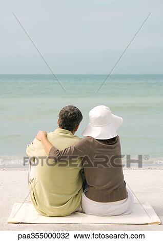 Couple sitting on beach, looking at sea, rear view View Large Photo Image Stock Image - Couple sitting on beach, looking at sea, rear view. Fotosearch
