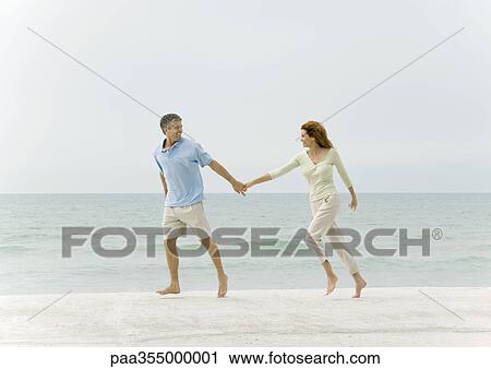 Stock Image - Couple walking hand in hand on beach. Fotosearch