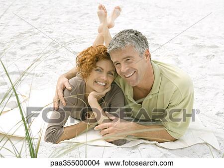 Picture - Mature couple lying on sand together. Fotosearch