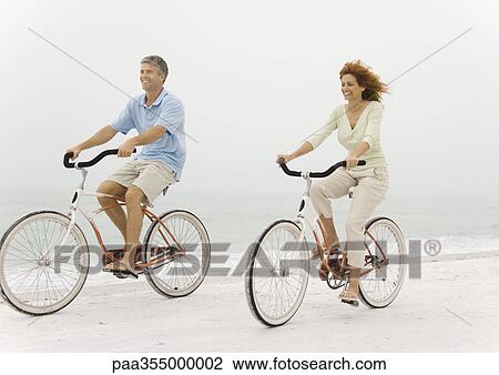 Mature Couple Riding Bikes On Beach Mature Couple Riding Bikes On Beach