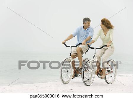 Stock Photograph - Mature couple riding bikes on beach. Fotosearch
