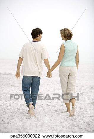 Mature couple walking on beach, holding hands, rear view View Large Photo Image Stock Image - Mature couple walking on beach, holding hands, rear view. Fotosearch