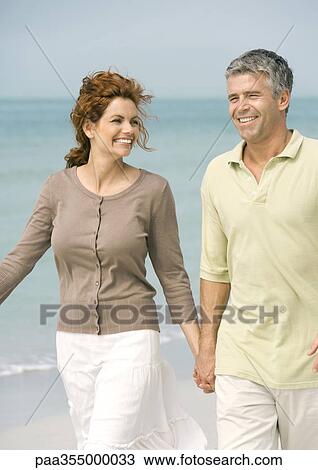 Stock Image - Mature couple walking on beach. Fotosearch