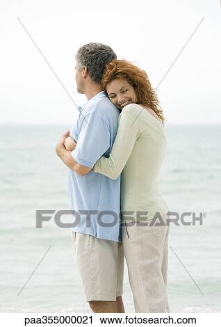 Stock Image - Mature couple, woman hugging man from behind. Fotosearch