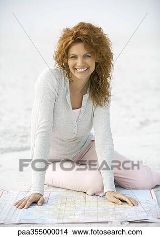 Picture - Mature woman sitting on sand with map. Fotosearch