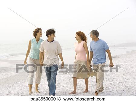 Stock Photo - Two mature couples walking on beach, holding hands . Fotosearch