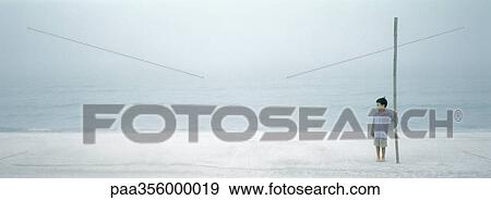 Boy standing on beach, holding big stick View Large Photo Image Stock Photo - Boy standing on beach, holding big stick. Fotosearch