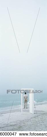 Stock Photo - Man standing looking at sea, seen through doorway on beach. Fotosearch