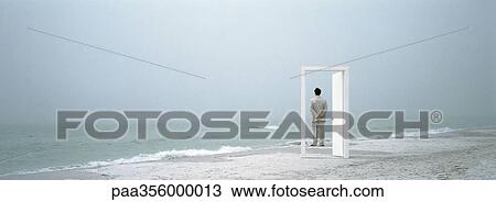 Stock Image - Man standing on beach, framed by doorframe. Fotosearch