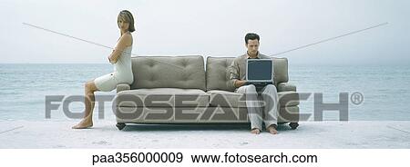 Stock Photo - On beach, couple sitting apart on sofa. Fotosearch