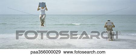 On beach, man and woman sitting holding up reading material in front of faces View Large Photo Image Stock Photo - On beach, man and woman sitting holding up reading material in front of faces. Fotosearch