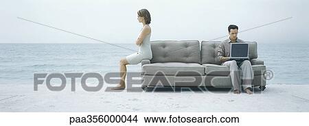 On beach, man using laptop on sofa while woman turns back to him View Large Photo Image Picture - On beach, man using laptop on sofa while woman turns back to him. Fotosearch