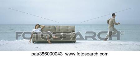 On beach, woman reclining on sofa while man runs away View Large Photo Image Stock Image - On beach, woman reclining on sofa while man runs away. Fotosearch