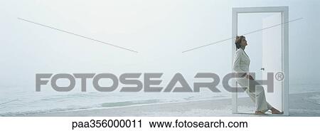Stock Image - Woman leaning against doorframe on beach. Fotosearch