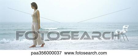 Stock Photo - Woman walking away from chair on beach. Fotosearch