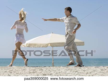 Couple chasing each other around parasol on beach View Large Photo Image Stock Photography - Couple chasing each other around parasol on beach. Fotosearch