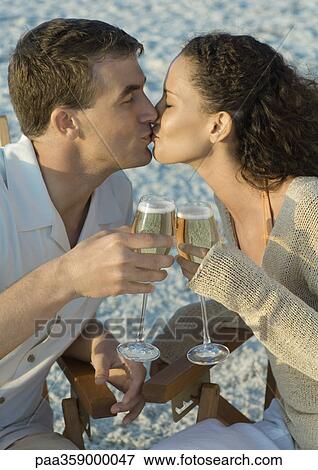 Stock Photo - Couple clinking glasses of champagne and kissing, on beach. Fotosearch