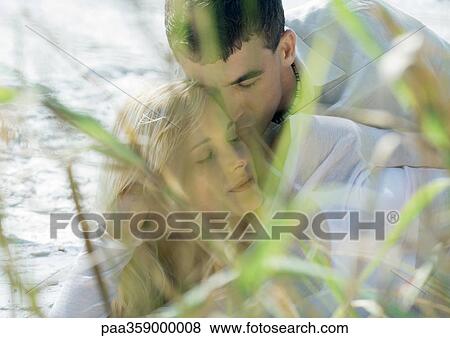 Stock Photo - Couple embracing, dune grass in foreground. Fotosearch