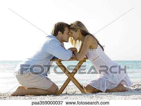 Couple kneeling on beach, nose to nose View Large Photo Image Stock Photo - Couple kneeling on beach, nose to nose. Fotosearch