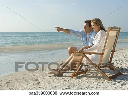 Couple sitting in deck chairs on beach View Large Photo Image Stock Photo - Couple sitting in deck chairs on beach. Fotosearch
