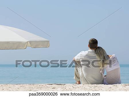 Couple sitting on beach, woman resting head on man's shoulder, rear view View Large Photo Image Stock Photograph - Couple sitting on beach, woman resting head on man's shoulder, rear view. Fotosearch