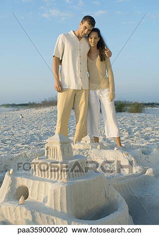 Couple standing on beach looking at sand castle View Large Photo Image Stock Image - Couple standing on beach looking at sand castle. Fotosearch