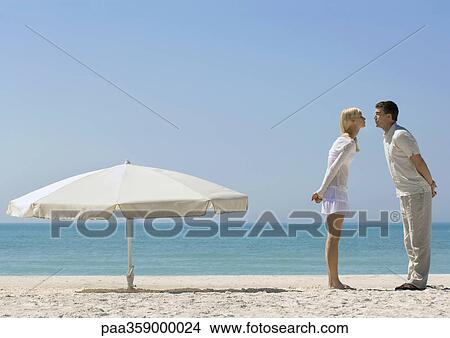 Couple standing on beach next to parasol, about to kiss View Large Photo Image Picture - Couple standing on beach next to parasol, about to kiss. Fotosearch
