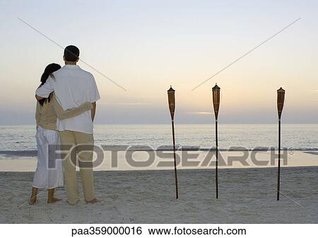 Couple standing on beach watching sunset View Large Photo Image Stock Photograph - Couple standing on beach watching sunset. Fotosearch