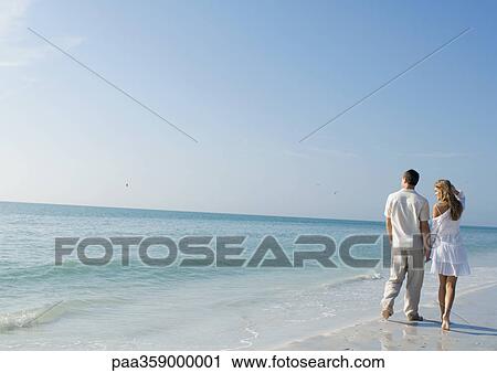Stock Image - Couple walking alongside water on beach. Fotosearch