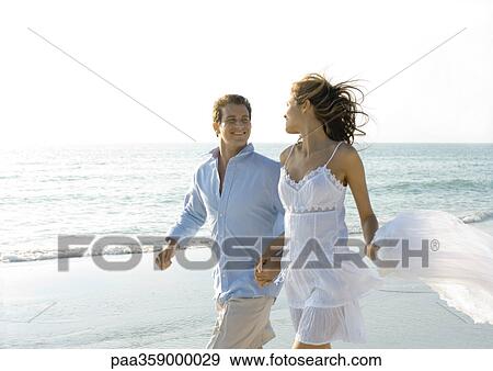 Couple walking on beach, smiling at each other View Large Photo Image Stock Photo - Couple walking on beach, smiling at each other. Fotosearch