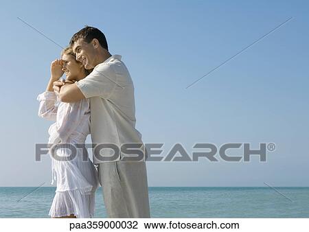 Stock Image - Man hugging woman on beach. Fotosearch