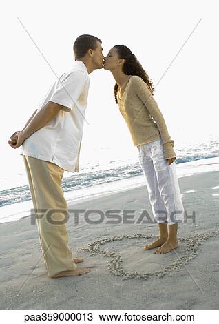 Newlyweds, woman standing inside heart drawn in sand, leaning forward to kiss husband View Large Photo Image Stock Image - Newlyweds, woman standing inside heart drawn in sand, leaning forward to kiss husband. Fotosearch